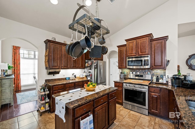 kitchen with stainless steel appliances, vaulted ceiling, decorative backsplash, dark brown cabinets, and light tile patterned floors