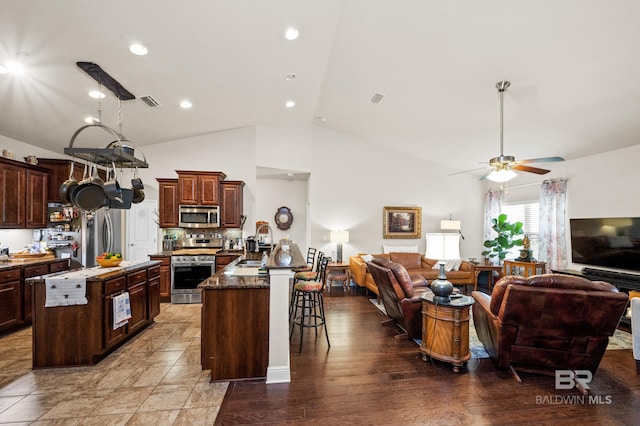 kitchen featuring tasteful backsplash, an island with sink, stainless steel appliances, and vaulted ceiling