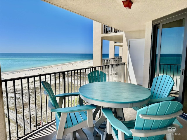 balcony with outdoor dining space, a view of the beach, and a water view