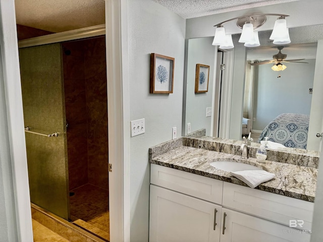 bathroom featuring a shower with door, ceiling fan, vanity, and a textured ceiling