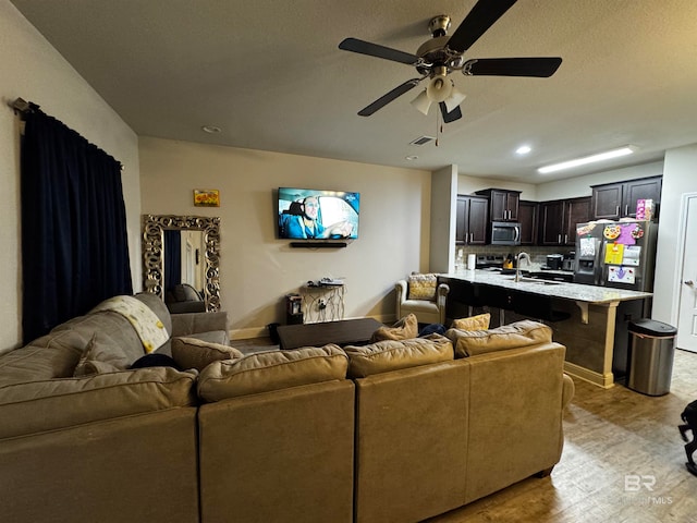 living room featuring ceiling fan, sink, and light hardwood / wood-style flooring