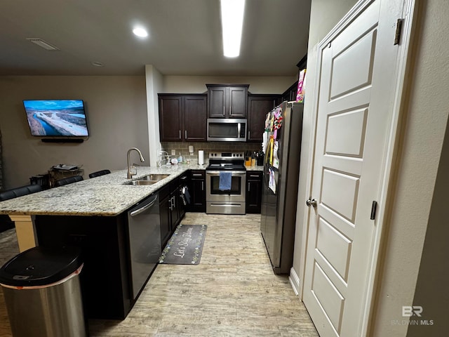 kitchen featuring kitchen peninsula, appliances with stainless steel finishes, tasteful backsplash, sink, and light hardwood / wood-style floors