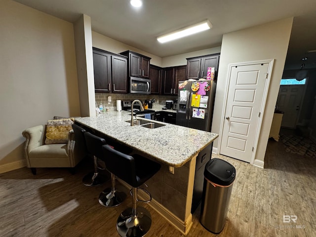 kitchen with decorative backsplash, appliances with stainless steel finishes, dark brown cabinets, sink, and hardwood / wood-style flooring