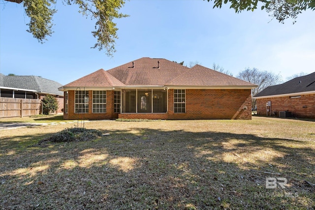 rear view of house with brick siding, a shingled roof, fence, a sunroom, and a yard