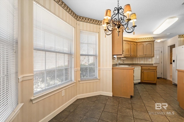 kitchen featuring white appliances, dark tile patterned flooring, decorative light fixtures, an inviting chandelier, and a sink