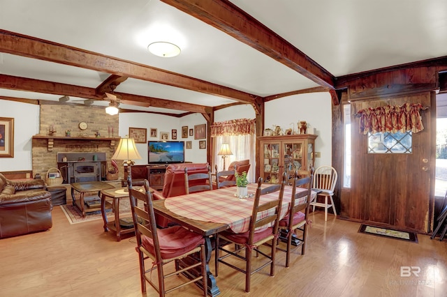 dining room featuring ceiling fan, light hardwood / wood-style floors, beamed ceiling, and a wood stove