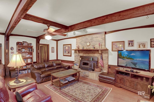 living room with beam ceiling, light hardwood / wood-style floors, ceiling fan, and a wood stove