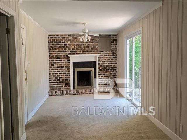 unfurnished living room with a brick fireplace, ornamental molding, wooden walls, carpet flooring, and ceiling fan