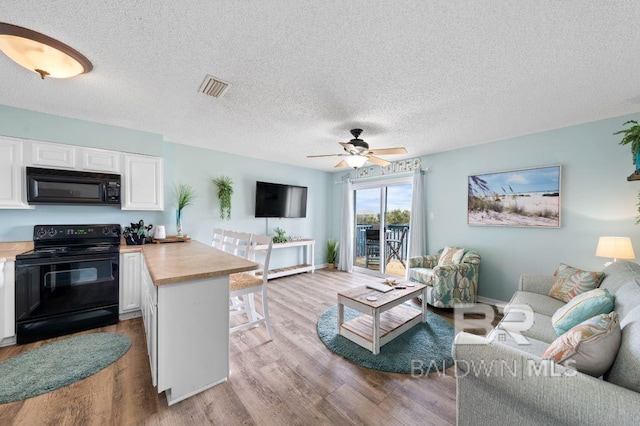 living room with visible vents, a textured ceiling, wood finished floors, baseboards, and ceiling fan