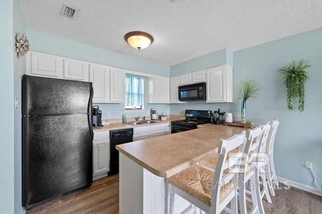 kitchen with a breakfast bar area, a peninsula, black appliances, and wood finished floors