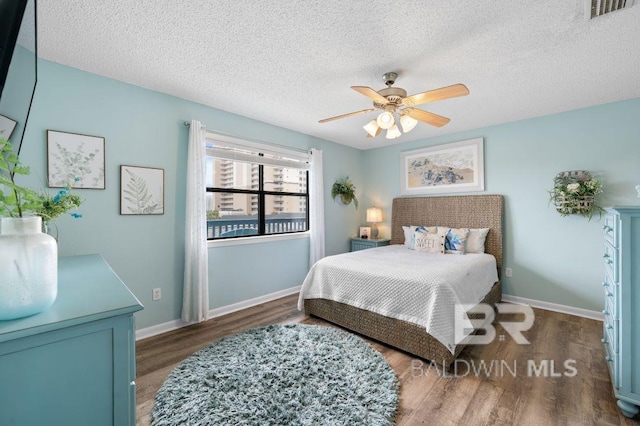 bedroom with visible vents, baseboards, a textured ceiling, and wood finished floors