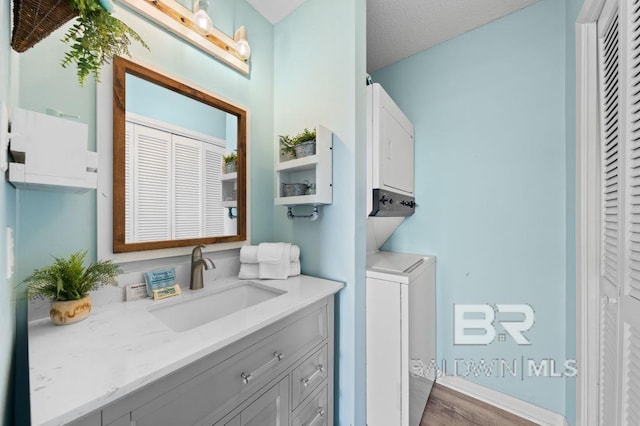 washroom featuring laundry area, a textured ceiling, stacked washer / drying machine, and a sink