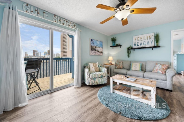 living room with ceiling fan, a view of city, wood finished floors, and a textured ceiling