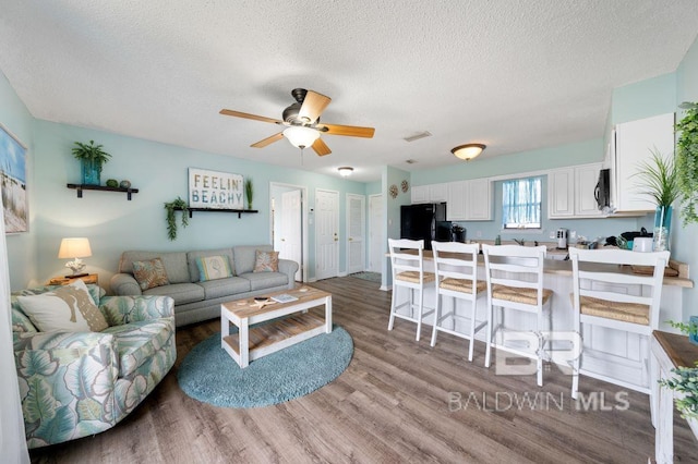 living area with visible vents, a textured ceiling, a ceiling fan, and wood finished floors