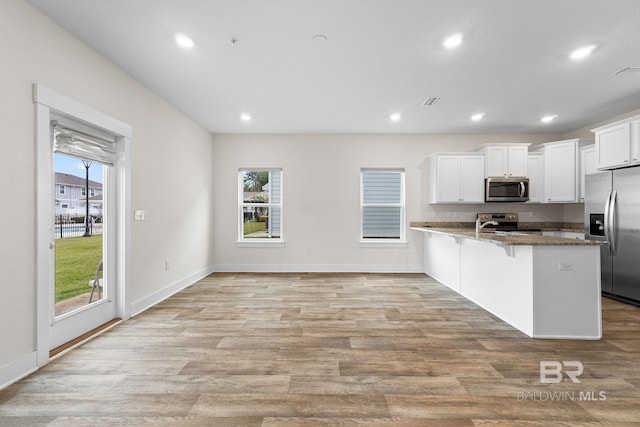 kitchen with appliances with stainless steel finishes, white cabinets, a kitchen bar, dark stone counters, and light wood-type flooring