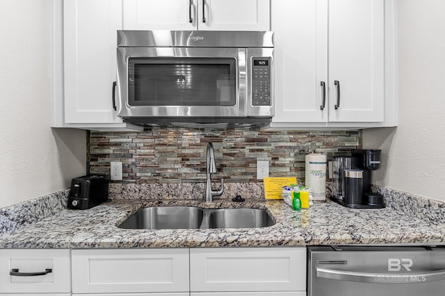 kitchen with white cabinets, sink, light stone countertops, tasteful backsplash, and stainless steel appliances