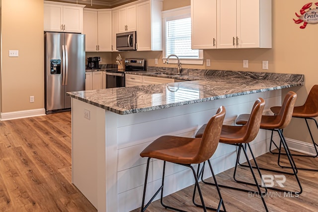 kitchen with a kitchen breakfast bar, dark stone counters, sink, white cabinetry, and appliances with stainless steel finishes