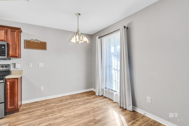 kitchen with stainless steel appliances, light hardwood / wood-style floors, a wealth of natural light, and a notable chandelier