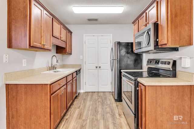 kitchen featuring a textured ceiling, sink, appliances with stainless steel finishes, and light hardwood / wood-style flooring