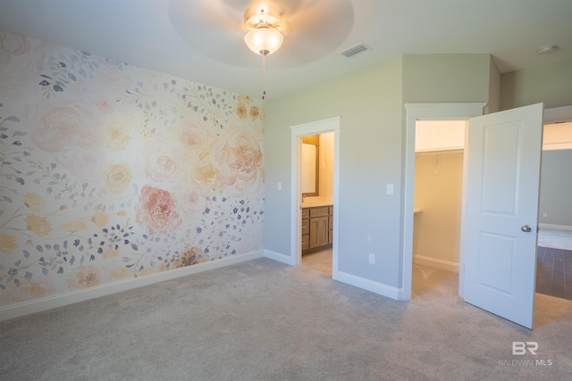 unfurnished bedroom featuring a spacious closet, ceiling fan, ensuite bathroom, light carpet, and a closet