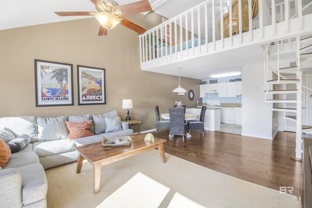 living area featuring baseboards, ceiling fan, light wood-style flooring, and a towering ceiling