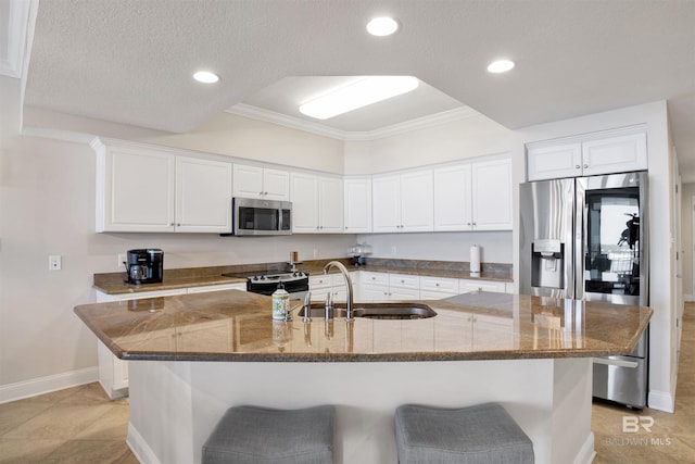 kitchen with appliances with stainless steel finishes, white cabinets, a sink, an island with sink, and a kitchen breakfast bar