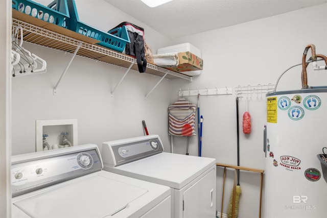 clothes washing area with laundry area, water heater, a textured ceiling, and washing machine and clothes dryer