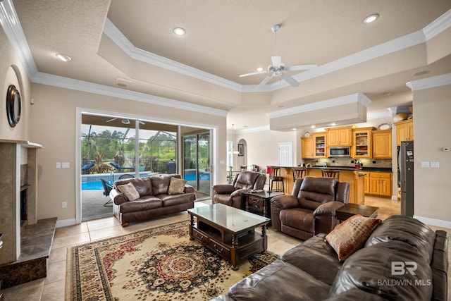 270 Cypress Lake Dr, Gulf Shores, AL 36542 - living room featuring a ceiling fan, ornamental molding, a raised ceiling, light tile patterned floors, and a fireplace