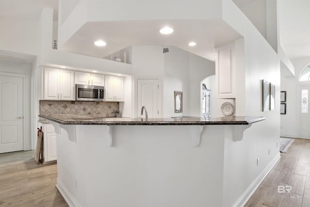 kitchen with white cabinetry, a kitchen breakfast bar, light hardwood / wood-style floors, decorative backsplash, and kitchen peninsula