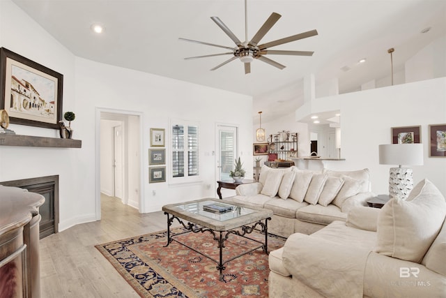 living room with ceiling fan, vaulted ceiling, and light wood-type flooring