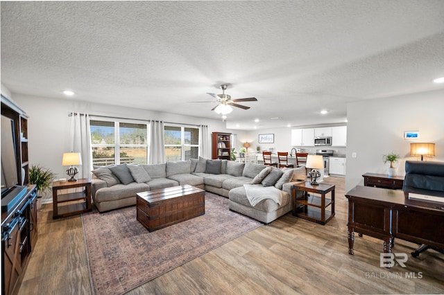 living room with ceiling fan, wood-type flooring, and a textured ceiling