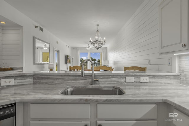 kitchen with light stone counters, stainless steel dishwasher, an inviting chandelier, white cabinetry, and sink