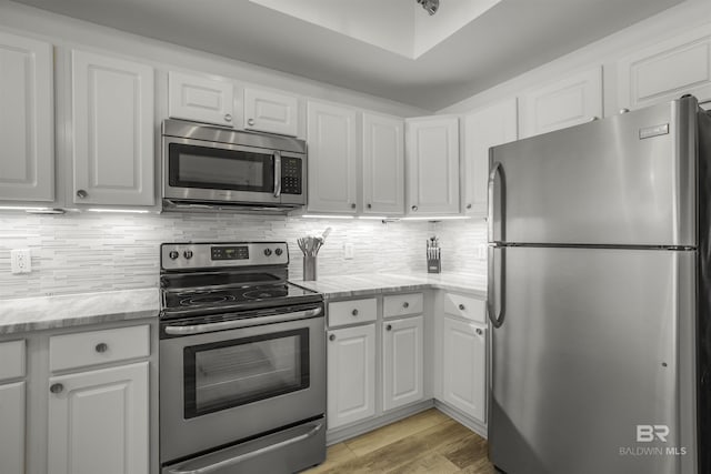 kitchen with white cabinetry, light wood-type flooring, light stone counters, and appliances with stainless steel finishes