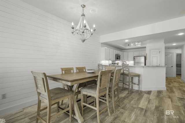 dining space featuring wood-type flooring, wooden walls, and a notable chandelier