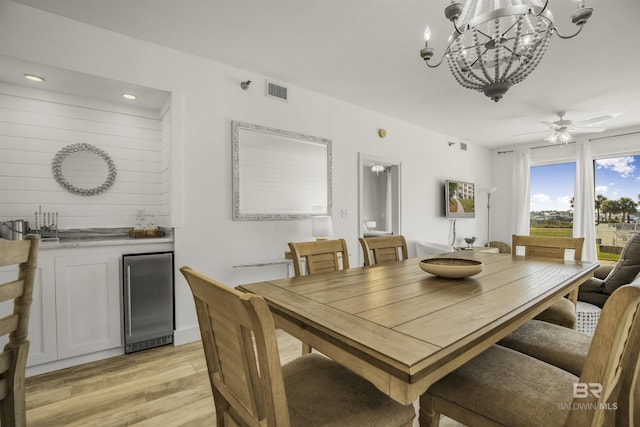 dining room with ceiling fan with notable chandelier, beverage cooler, and light hardwood / wood-style flooring