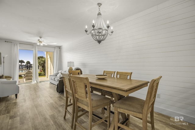 dining space featuring wooden walls, ceiling fan with notable chandelier, and hardwood / wood-style flooring