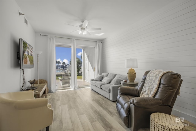 living room with wood walls, ceiling fan, and light hardwood / wood-style flooring