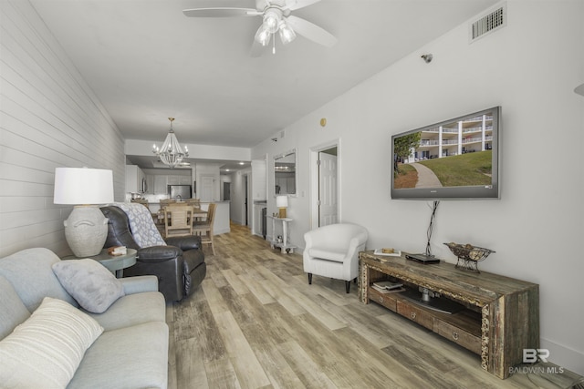 living room featuring ceiling fan with notable chandelier, wood walls, and hardwood / wood-style floors