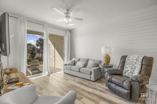 living room with wood walls, ceiling fan, and light hardwood / wood-style flooring