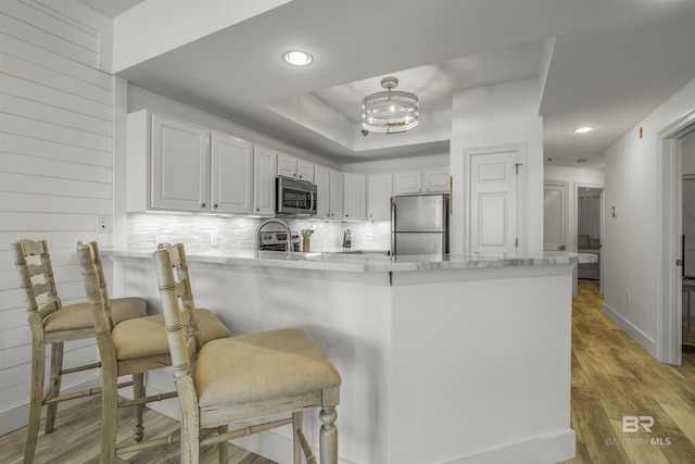 kitchen featuring a breakfast bar area, appliances with stainless steel finishes, kitchen peninsula, decorative backsplash, and white cabinetry