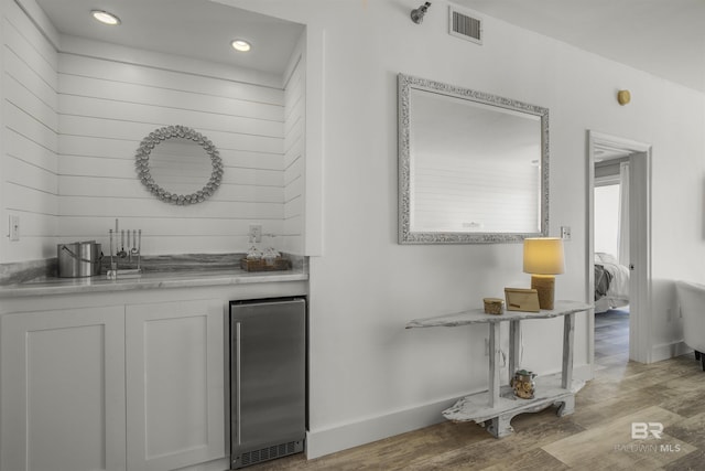 bar with white cabinets, light wood-type flooring, and stainless steel fridge