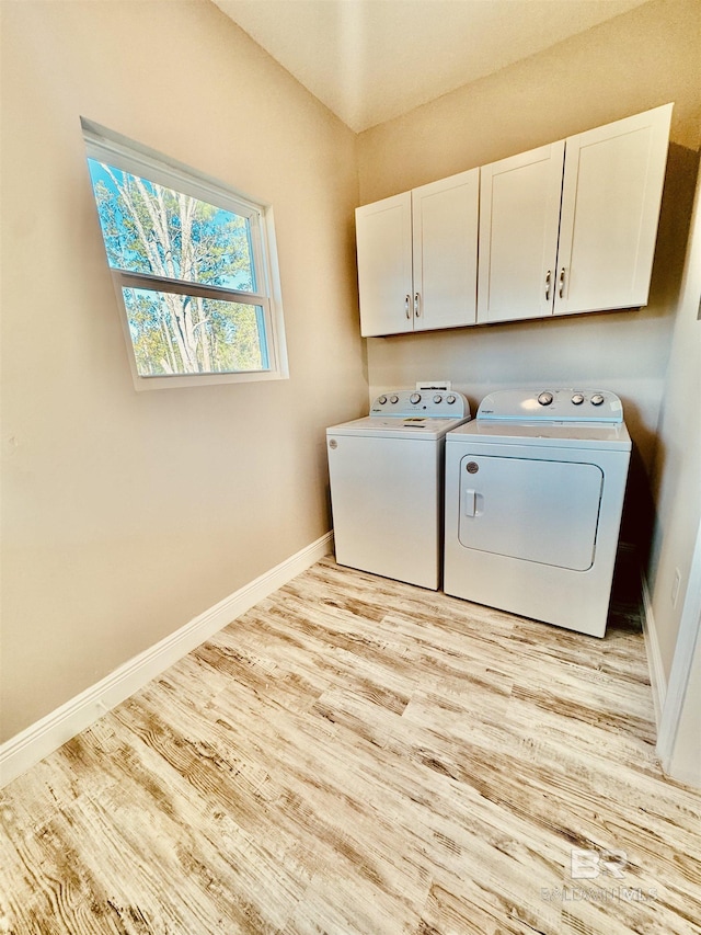 washroom featuring cabinets, washing machine and clothes dryer, and light wood-type flooring