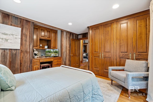 bedroom featuring light wood-type flooring, a closet, wooden walls, and crown molding