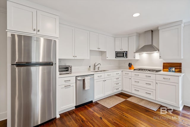 kitchen with white cabinets, stainless steel appliances, dark hardwood / wood-style flooring, sink, and wall chimney range hood