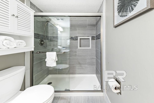 bathroom with toilet, a shower with door, and a textured ceiling