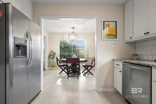 kitchen featuring appliances with stainless steel finishes, light stone counters, a notable chandelier, white cabinets, and hanging light fixtures