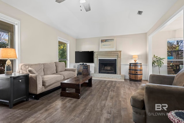 living room with ceiling fan, dark wood-type flooring, vaulted ceiling, and a brick fireplace