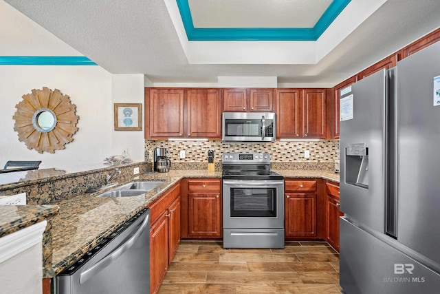 kitchen featuring dark stone countertops, appliances with stainless steel finishes, light wood-type flooring, sink, and tasteful backsplash