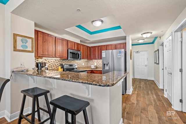 kitchen with stainless steel appliances, light hardwood / wood-style flooring, kitchen peninsula, decorative backsplash, and dark stone counters