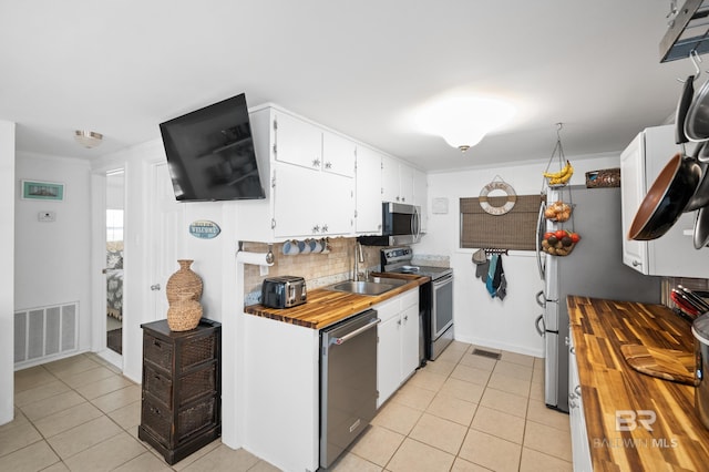 kitchen featuring white cabinets, wood counters, light tile patterned floors, and stainless steel appliances